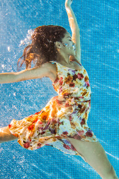 Woman in floral dress floating underwater in a swimming pool