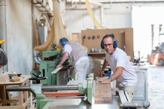 Coworkers wearing earmuff while sawing wood in machine at factory