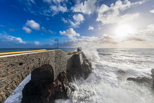 Heavy waves crash against the stone pier at Cais da Ponta do Sol