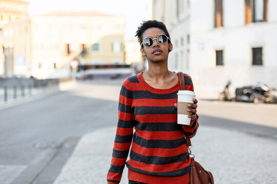 Portrait of young woman with coffee to go wearing sunglasses and striped pullover