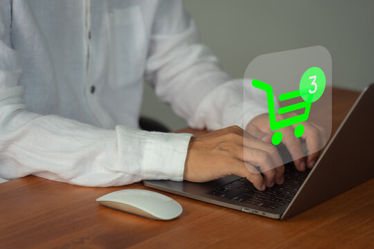 Man typing on a laptop with a digital green shopping cart icon. Online shopping, e-commerce, and internet buying concept.