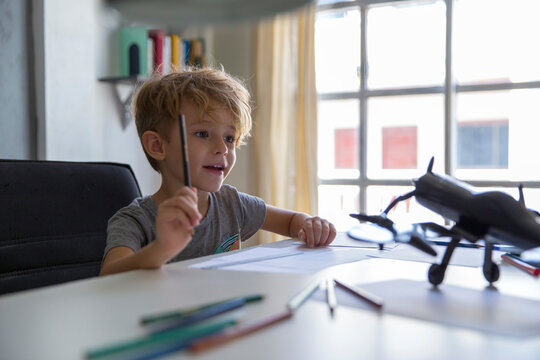Surprised boy with pencil looking at model airplane