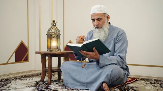 Elderly muslim man with long white beard reading quran with prayer beads