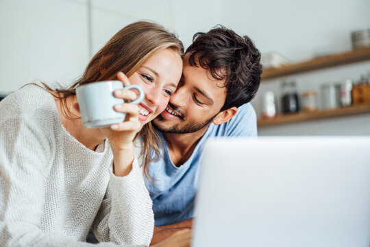 Happy man embracing girlfriend looking at laptop in kitchen