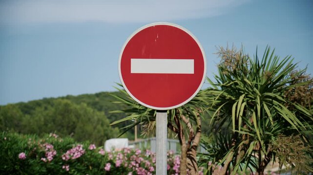 Red no entry traffic sign standing against a sunny natural background with greenery and blue sky
