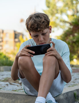 Boy deeply focused on playing smartphone game outdoors. Mobile technology has become natural part of modern childhood, daily routine and digital entertainment