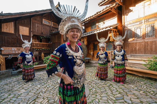 China, Guizhou, happy Miao women wearing traditional dresses and headdresses standing on village square