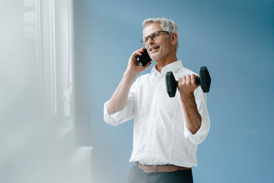 Successful manager using smartphone and training with a dumbbell