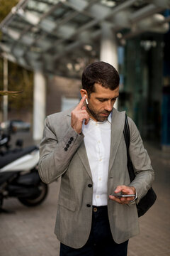 Businessman with cell phone and bluetooth earbuds in the city