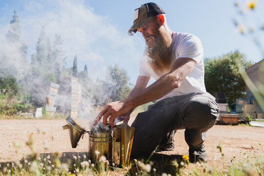 Bearded beekeeper prepares a smoker at an outdoor apiary