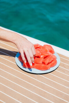 Hand taking a slice of watermelon on a yacht deck in summer