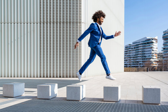 Playful businessman jumping on concrete block
