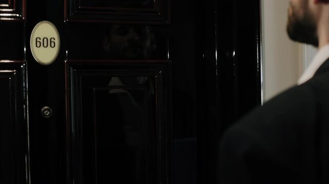 Over-shoulder motion shot of person using right fist to knock on closed glossy black raised-panel door marked 606
