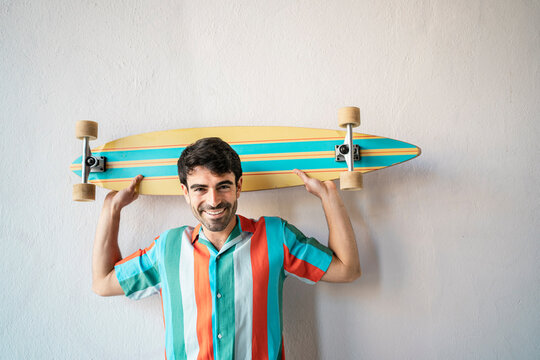 Happy handsome man with longboard in front of wall