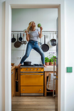 Carefree woman standing on stove enjoying dancing in kitchen