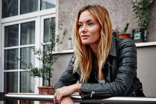 Confident young woman wearing biker jacket leaning on balcony railing