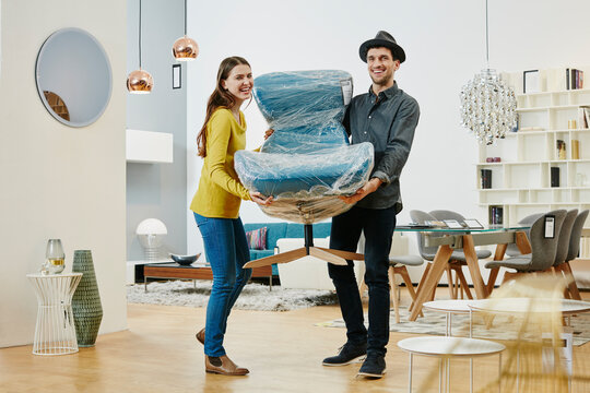 Happy couple carrying new arm chair out of furniture store