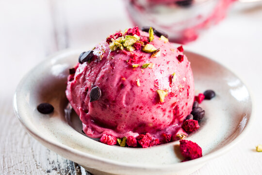 Plate of vegan sugarfree nice cream with raspberries, bananas, sprinkled pistachios and chocolate