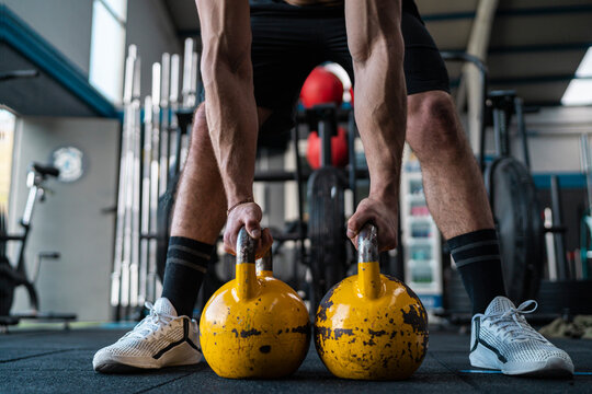 Muscular male athlete holding kettlebells in gym