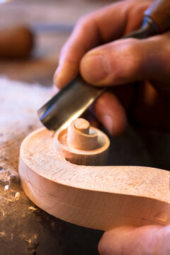 Male violin maker carves a wooden scroll in his workshop