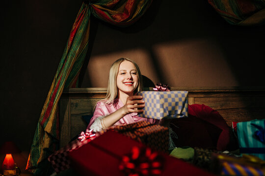 Happy woman holds a birthday gift in bed in the morning