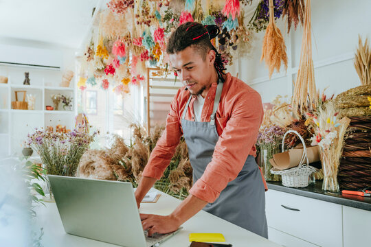 Young store owner using laptop at desk in flower shop