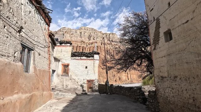 Forward walking POV down a narrow alley past a whitewashed house with carved window, Chhusang village, Upper Mustang, Nepal