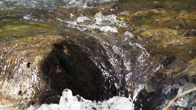 4x slow motion close-up video of turbulent mountain river with crystal-clear water tumbling over small rapid of exposed rocks, boulders. Angle view of current directly above, nature footage, 30 fps