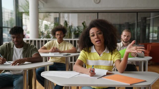 Four multiracial students in classroom lesson African American student girl raising arm asking talking to tutor lecturer study learn class in high school university college studying educate learning