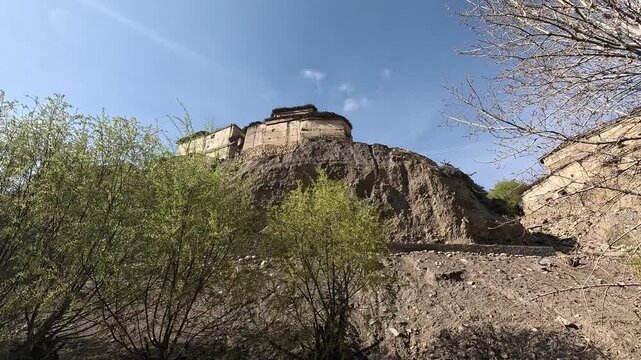 Low-angle shot of a mud-brick house perched on an eroded bluff above a dry riverbed, Tetang village, Upper Mustang, Nepal