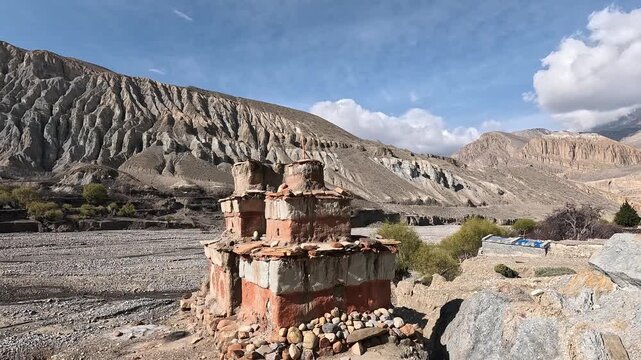Orbiting shot of a weathered red and white painted Buddhist chorten below eroded mountains, Chhusang, Upper Mustang, Nepal