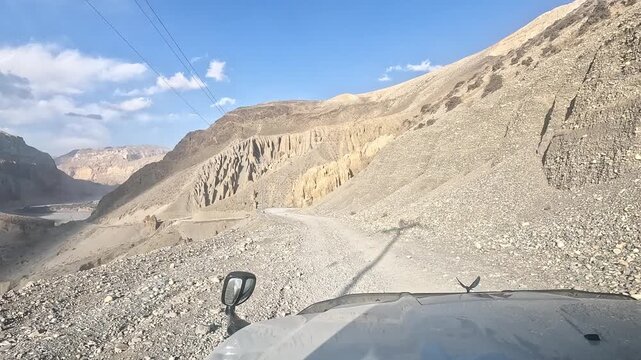 Driving POV below dramatic banded cliffs of ochre and grey eroded strata, Chuksang, Nepal