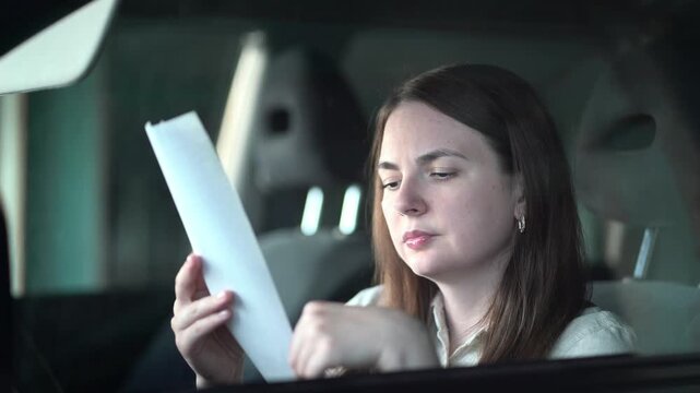 Young woman seated in a car intently examines a paper receipt detailing expensive shopping purchases while reviewing her expenses and budget.