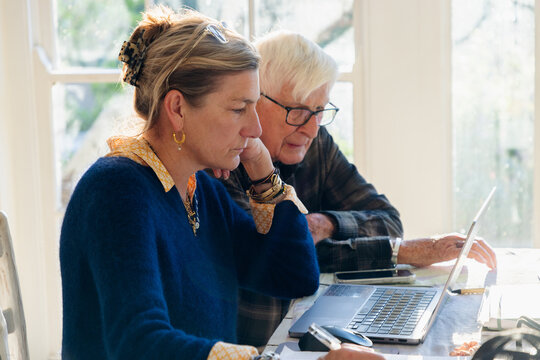 adult daughter helping her elderly father with his finances using laptop
