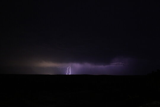 Rayos verticales cayendo sobre el horizonte en tormenta nocturna lejana. Paisaje dram&aacute;tico con cielo morado, nubes oscuras y amplio espacio negativo.