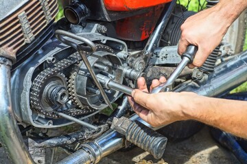 Fototapeta premium Close-up of a motorcycle retro iron dirty engine with chain repair using a hand tool. The mechanic performs maintenance, adjustment and assembly of engine parts during repair.