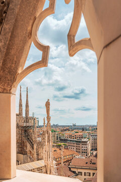 Scenic view of Milan rooftops framed through a gothic marble cathedral arch.