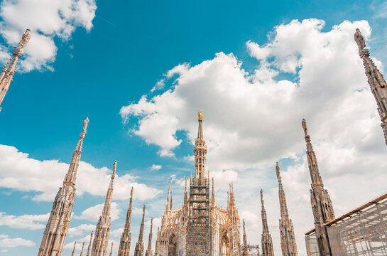 Looking up at multiple gothic marble spires of Milan Cathedral against sky.