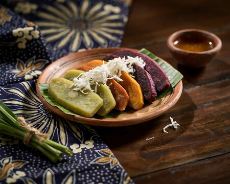 Traditional indonesian steamed snacks with grated coconut on earthenware plate and batik fabric background.