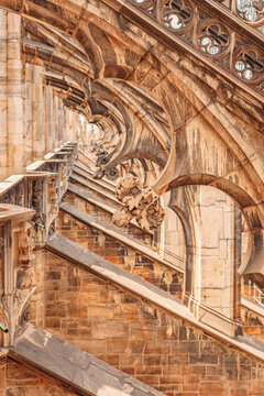 Intricate gothic flying buttresses and marble stairs on Milan Cathedral rooftop.
