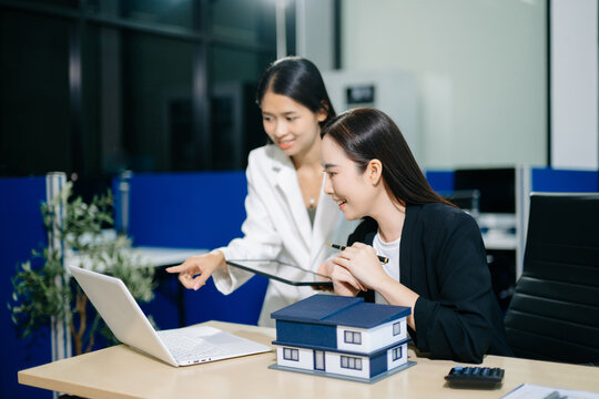 Professional Asian real estate consultant presenting a house model to a client during a property investment meeting in a modern office.