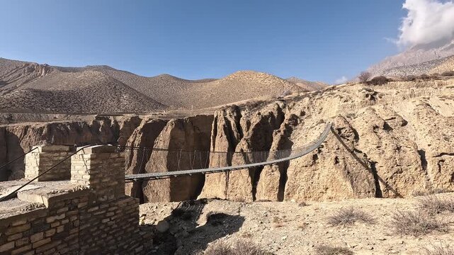 Suspension bridge towards Ghyakar village spanning rocky ravine, Upper Mustang Nepal
