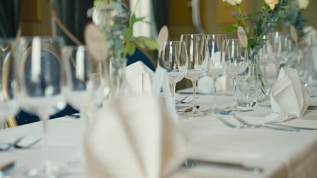 An elegantly arranged wedding reception table is set with glassware, folded napkins, floral details, and soft natural light, creating a refined atmosphere of celebration and formal dining.