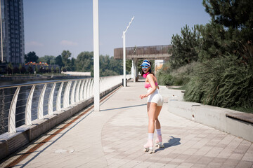 Obraz premium Young woman roller skating on a sunny waterfront promenade wearing retro outfit and visor, smiling and looking back while enjoying outdoor fitness and leisure