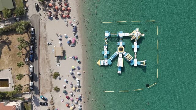 Floating inflatable playground in the sea, Water park in Pefkohori beach turquoise shallow waters, Halkidiki, Overhead aerial view