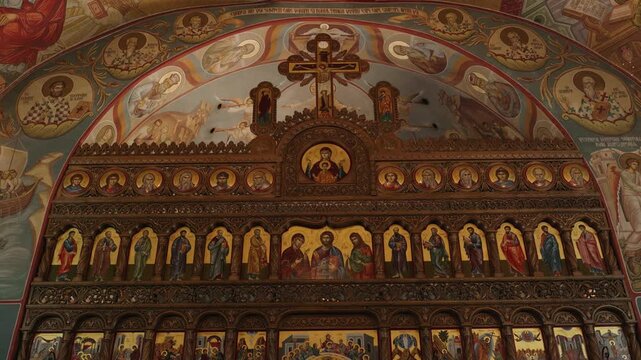 Front-facing view of an ornate Orthodox church iconostasis featuring traditional Christian icons, decorative wood carvings, colorful Byzantine frescoes, and a central cross above the altar.