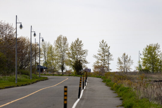 Gaspesie, Canada, 31 May 2026 : A paved path with streetlights and bollards curves through a green space under an overcast sky.