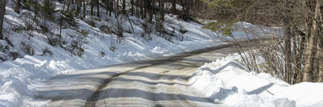 Canada, 12 April 2026 : Unpaved road covered in snow and ice with tire tracks through a winter forest