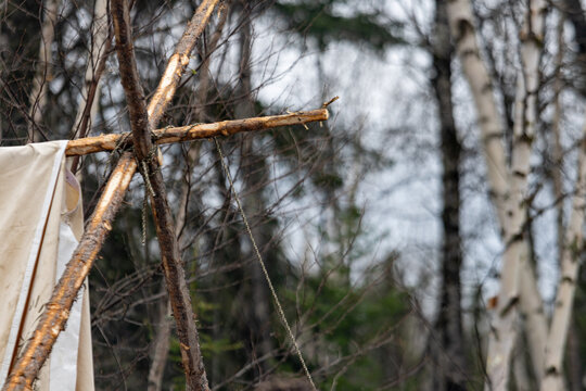 Parents, Quebec, 19 May 2026 : Rustic wooden structure made of branches tied together supports a piece of fabric in a forest.