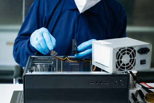 Professional technician wearing a mask and gloves installs a power supply unit into a PC case, showcasing hardware assembly, repair, and tech maintenance.